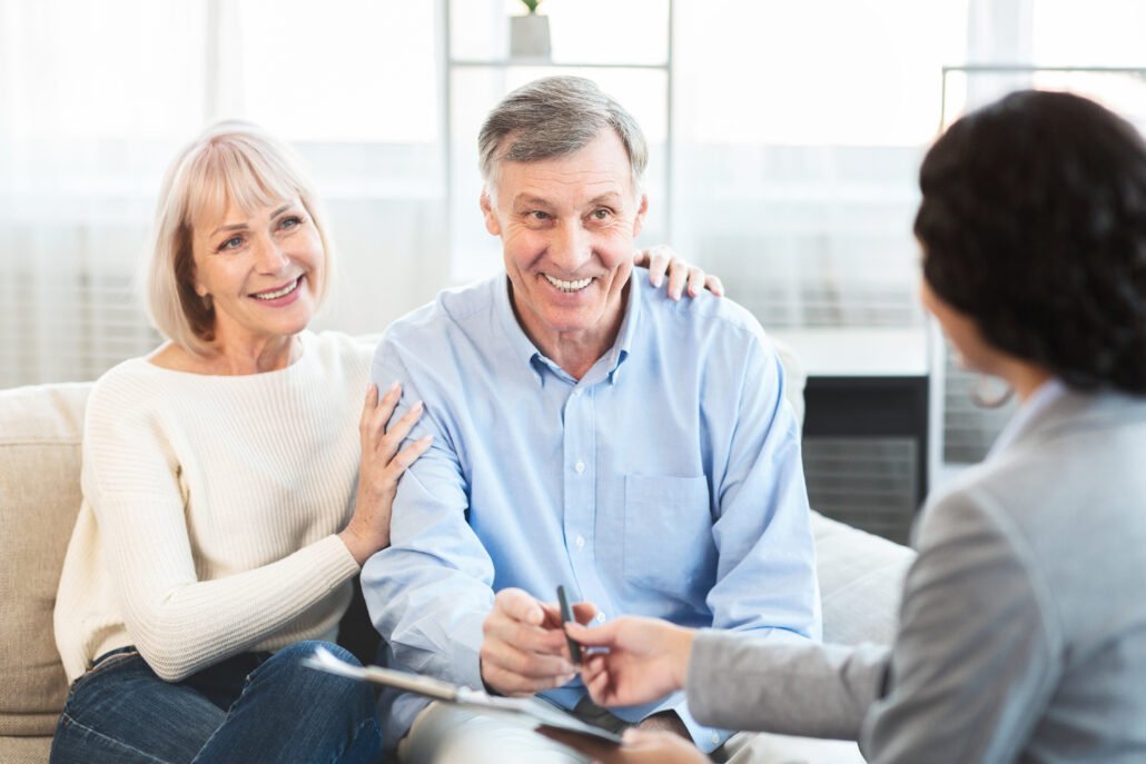 Happy senior couple consulting with female financial advisor at home, signing papers